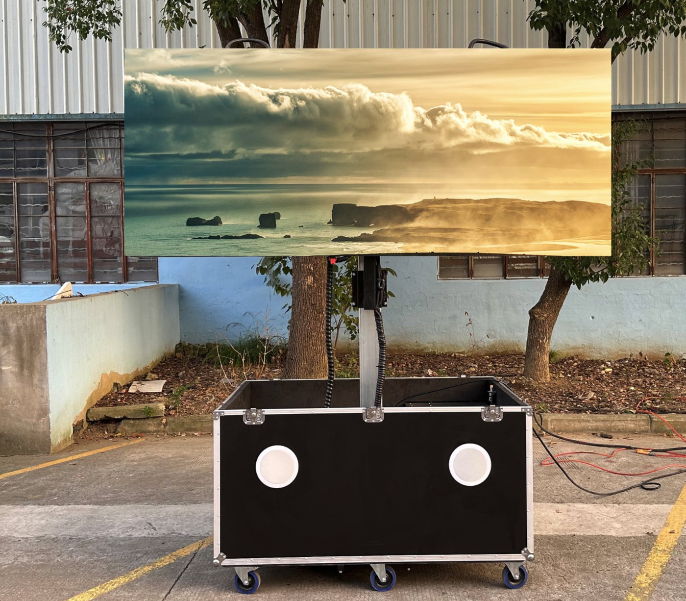 Mobile LED display on a lift pole with flight-case base and built-in speakers, shown outdoors — manufacturer reference