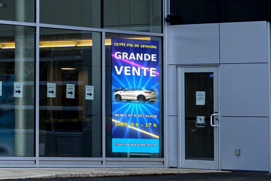 Écran DEL suspendu derrière la vitrine d’une concession automobile, face à la rue