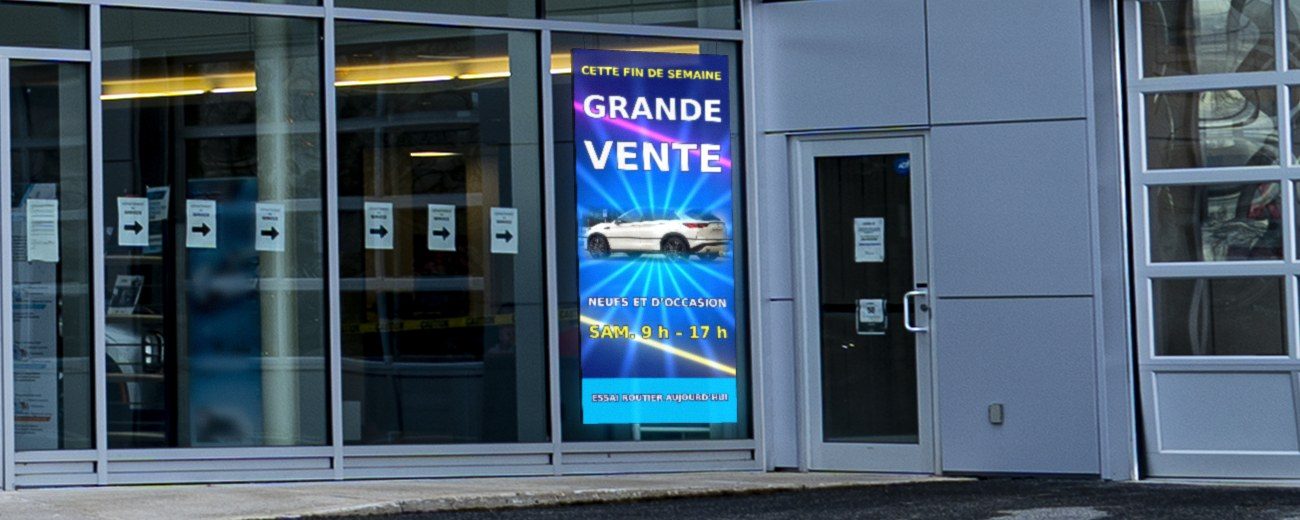 Écran DEL suspendu à l’intérieur, derrière la vitrine d’une concession automobile, face à la rue